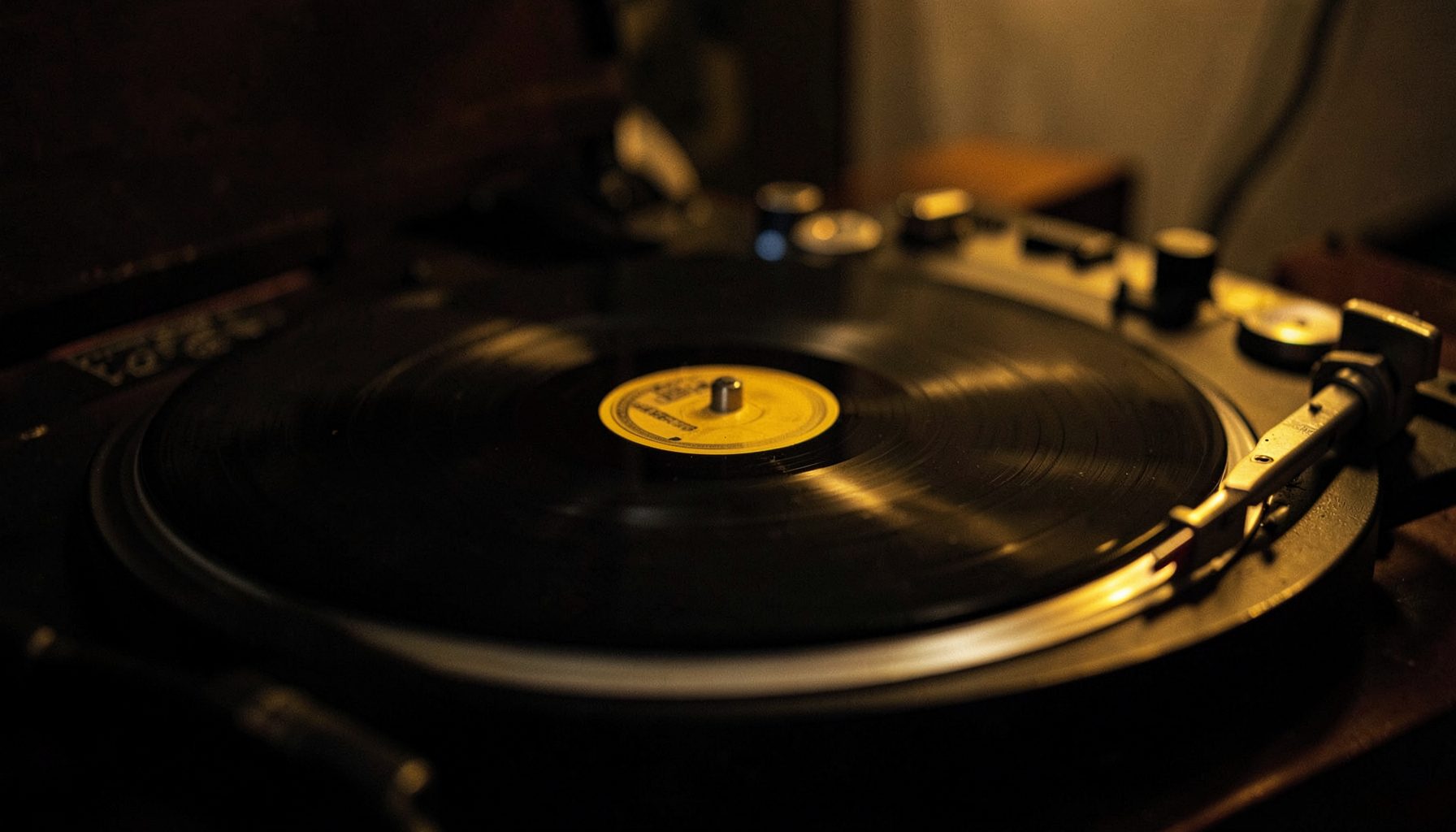 Disco de vinilo sobre un tocadiscos con una aguja posada, luz tenue y cálida, tonos negros y dorados, atmósfera íntima