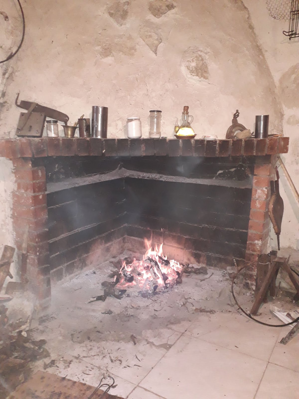 Chimenea rústica de ladrillo con un pequeño fuego encendido, varios recipientes sobre la repisa, luz cálida