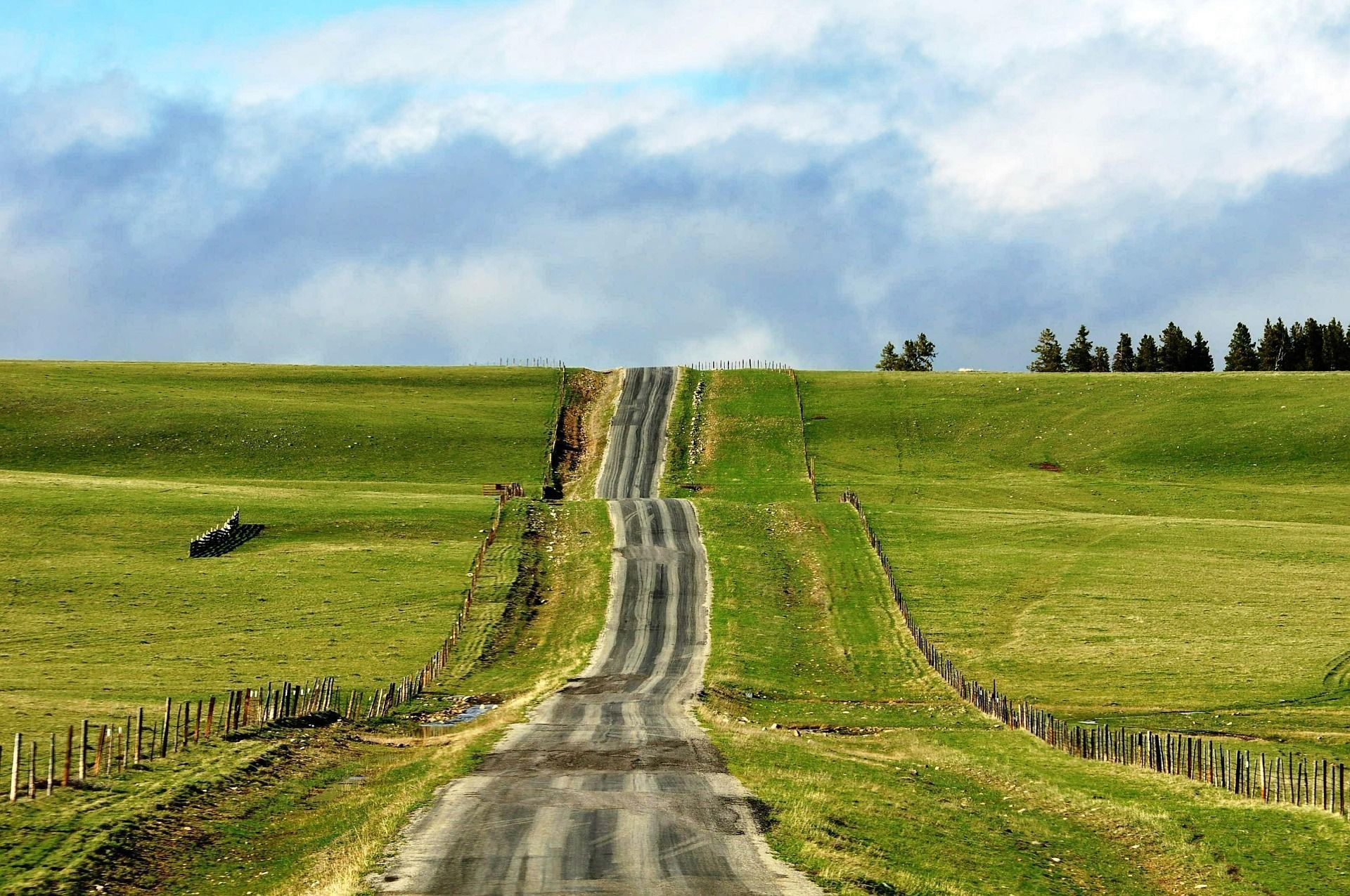 Camino rural que serpentea entre colinas verdes bajo un cielo parcialmente nublado, paisaje sereno